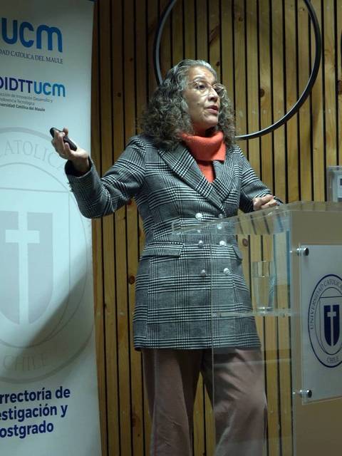 Una mujer con gafas y cabello rizado está dando una charla en un auditorio.