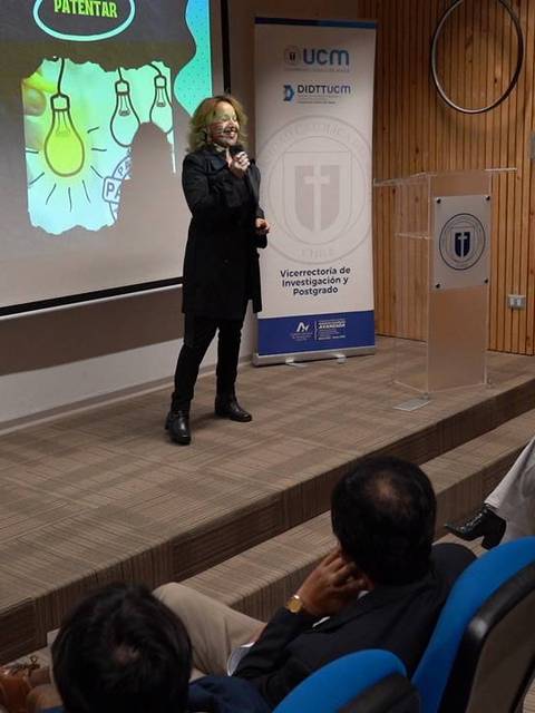 Una oradora presenta un tema con apoyo visual en una conferencia.