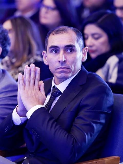 Un hombre con traje oscuro observa atentamente mientras se encuentra sentado en un evento.