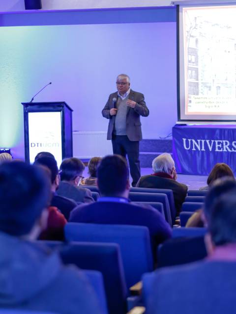 Un orador presenta en un auditorio universitario mientras la audiencia lo escucha atentamente.