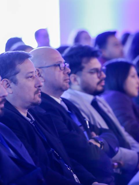 Un grupo de personas sentado en un evento, prestando atención, con iluminación azul de fondo.