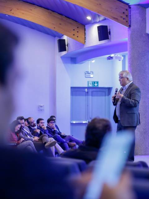 Un orador presenta a un público en un auditorio moderno durante un evento.