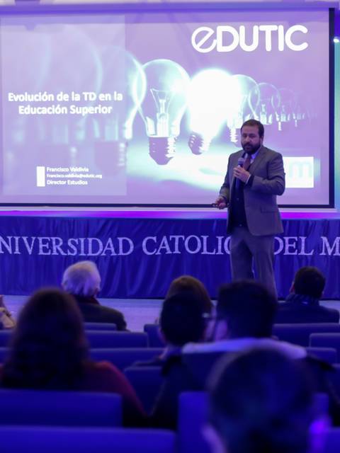 Un ponente presenta sobre la evolución de la tecnología en la educación superior en un auditorio.