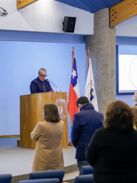 Un hombre habla desde un podio en un evento formal con la asistencia de varias personas.