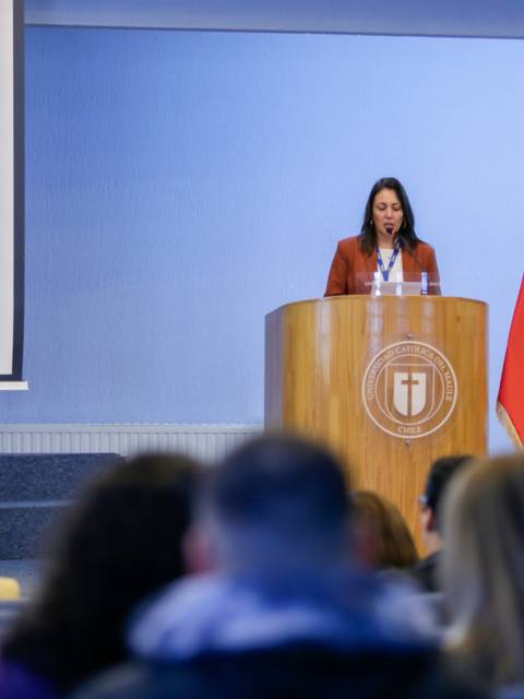 La imagen muestra a una mujer hablando desde un podio en un evento en Chile, con banderas y un público presente.