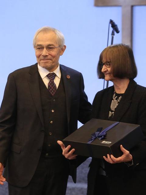 Dos personas sonríen mientras sostienen un regalo en un evento formal.