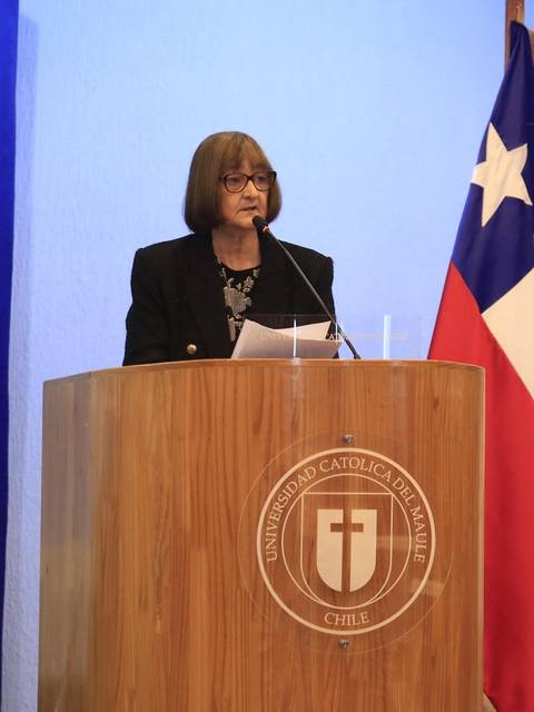Una mujer de pie en un podio presenta en un evento de la Universidad Católica del Maule en Chile.