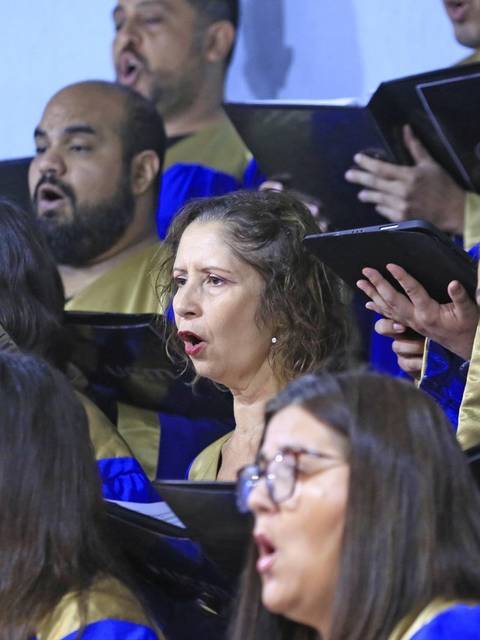 Un grupo de personas cantando en un coro, con partituras en las manos y vestimenta colorida.