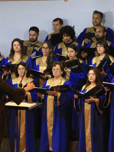 Un coro de personas canta mientras son dirigidos por una directora.