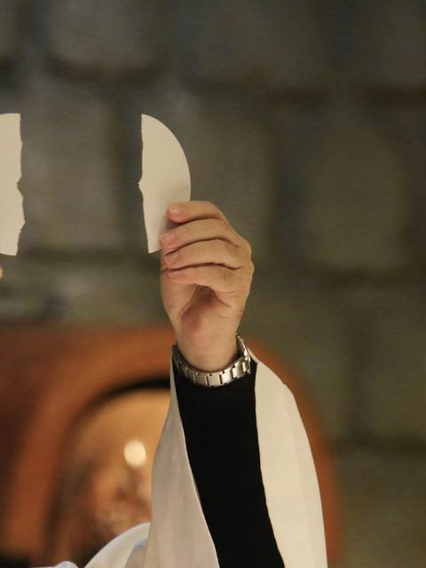 Un sacerdote sostiene dos piezas de un objeto mientras se lleva a cabo una ceremonia religiosa.