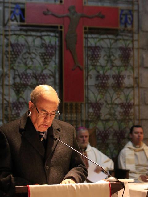 Un hombre lee en un altar con una cruz grande de fondo durante una ceremonia religiosa.