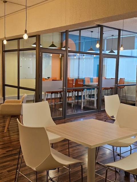 Una sala moderna con mesas y sillas, iluminada con luces colgantes.