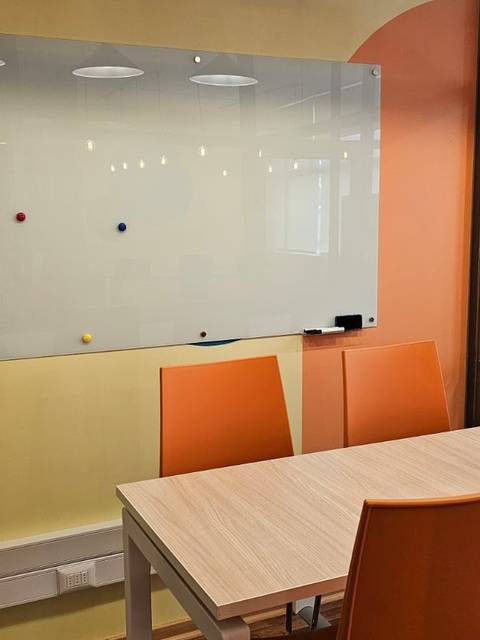 Una sala de reuniones con una mesa y sillas naranjas, y una pizarra blanca en una pared de colores.