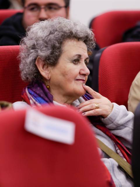 Un grupo de personas sentadas en un salón, con una mujer de cabello rizado en primer plano.