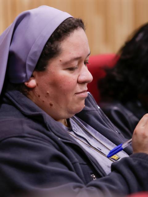 Una mujer con hábito religioso está escribiendo notas en una reunión.
