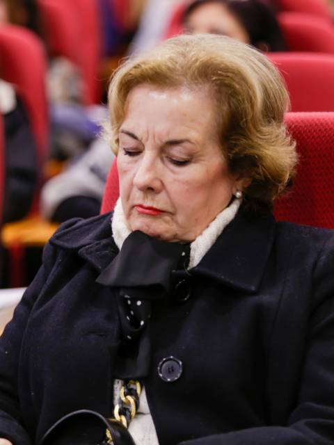 Una mujer mayor escribe en un cuaderno mientras escucha atentamente en una conferencia.