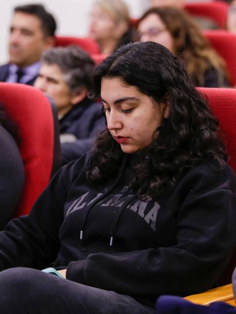 Un grupo de personas escucha atentamente en un evento, mientras una joven toma notas.