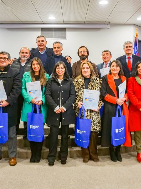 Un grupo de personas posando en un evento de entrega de certificados, sosteniendo sus diplomas y bolsas azules.