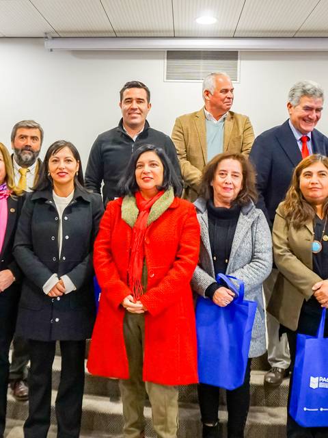 Grupo de personas posando en un evento con bolsas azules en una sala de conferencias.