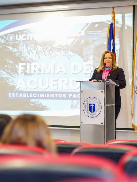 Una mujer está dando un discurso en un evento formal de firma de acuerdos en una sala de conferencias.
