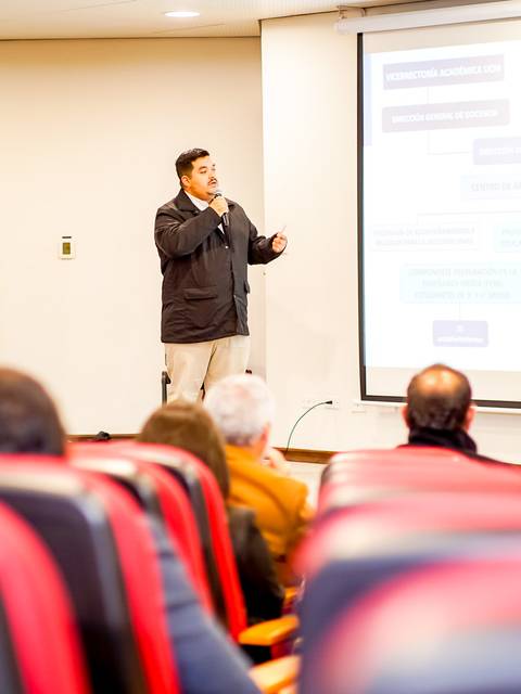 Un presentador habla frente a un público en una sala de conferencias.