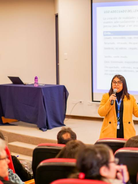Una mujer habla frente a un grupo durante una presentación en un salón de actos.