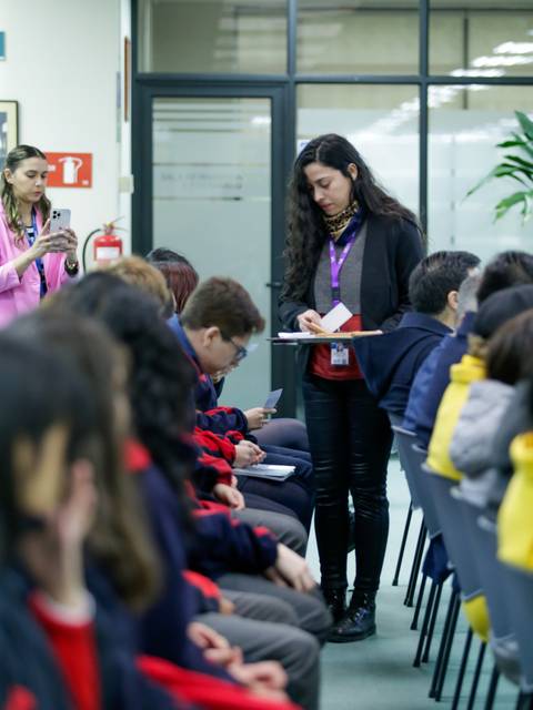 Una mujer con una tablet se encuentra de pie frente a una audiencia sentada en un salón.