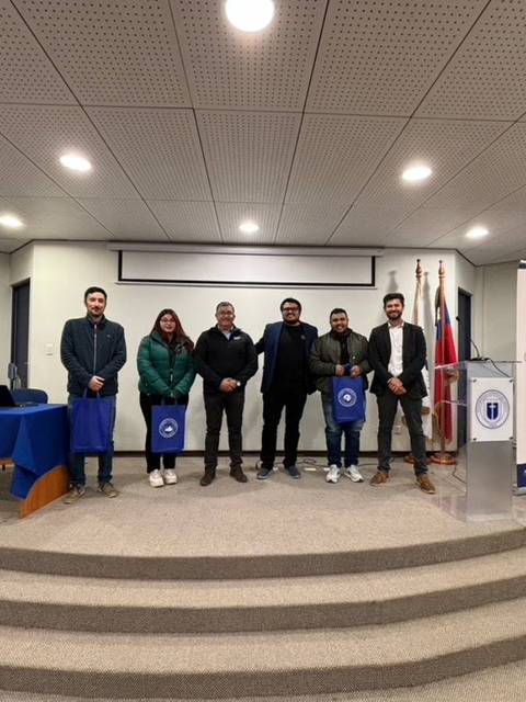 Un grupo de seis personas posando en un escenario durante un evento en una sala con banderas.