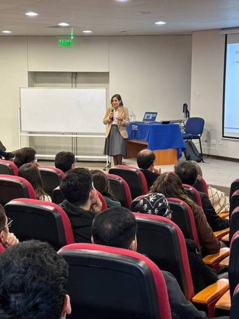 Una oradora presenta en un auditorio a un público atento.