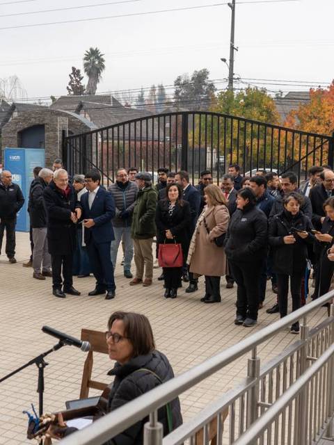 Un grupo de personas se congrega en la entrada de un recinto, mientras una mujer toca un instrumento musical.
