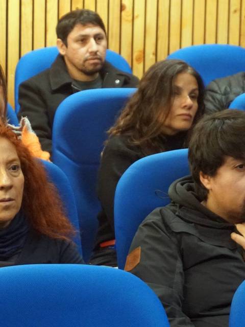 Un grupo de personas sentadas en sillas azules en un ambiente interior.