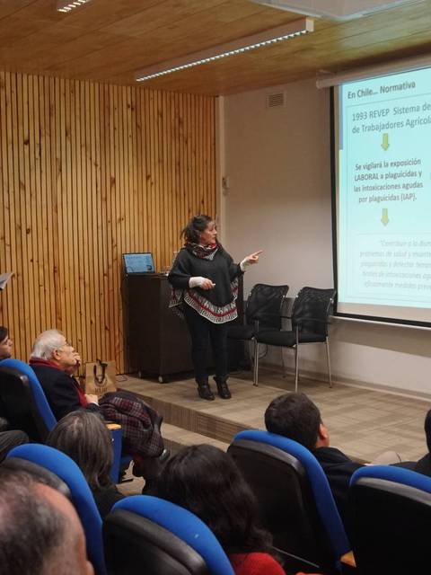 Una conferencia en un auditorio donde una mujer presenta información a un grupo de personas sentadas.