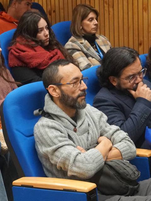 Un grupo de personas sentadas en una sala, prestando atención a la presentación.