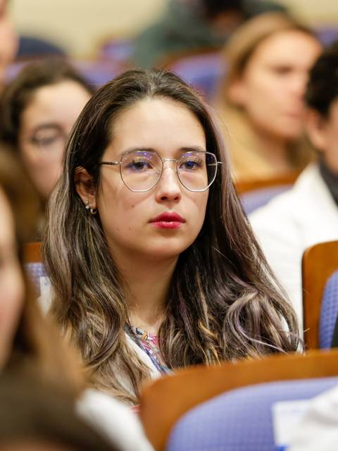 Una joven con gafas observa atentamente a un grupo de personas en una conferencia.