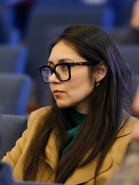 Una mujer con gafas sentada en un auditorio, observando atentamente.