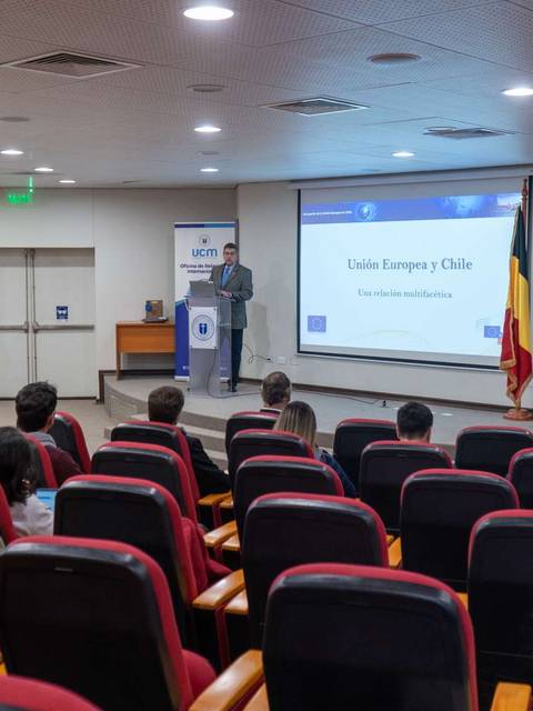 Un orador presenta un evento sobre la Unión Europea y Chile ante una audiencia en un auditorio.