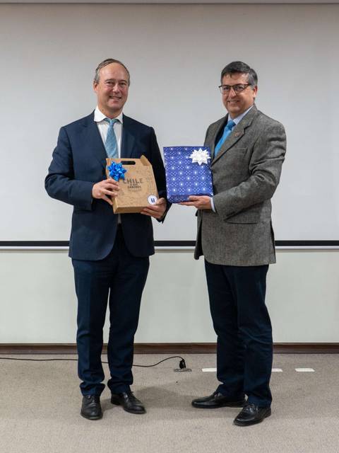 Dos hombres en una presentación sosteniendo regalos en un ambiente formal.