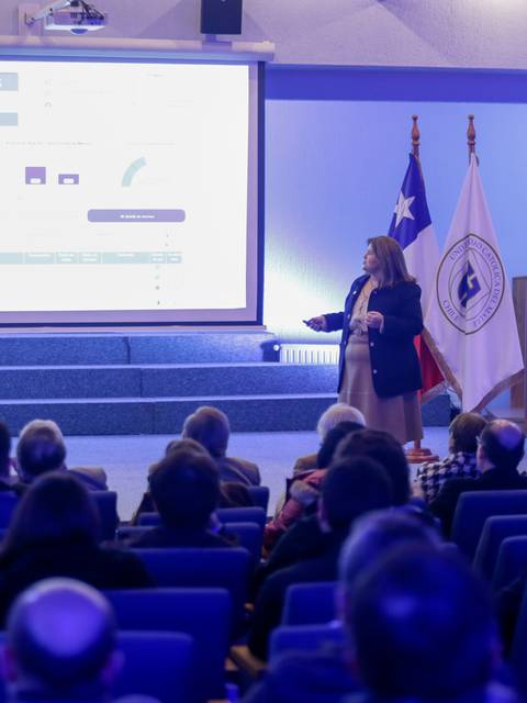 Una presentación en un auditorio con un público atento y un proyector mostrando información en pantalla.