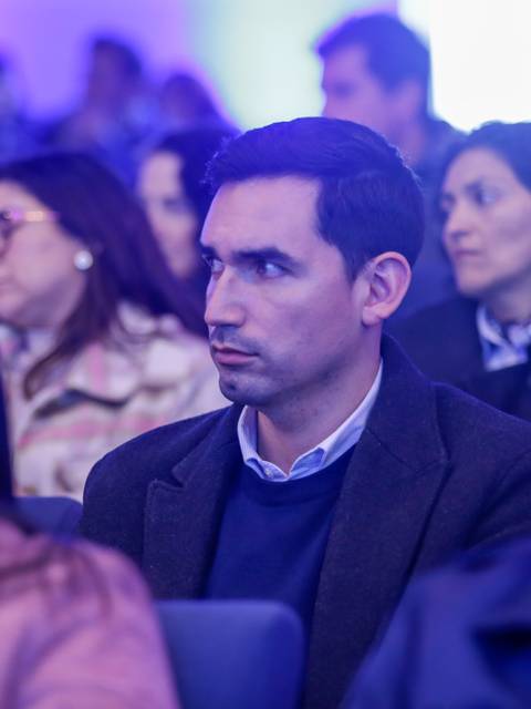 Un grupo de personas asistiendo a un evento, con un enfoque en un hombre sentado en primer plano.