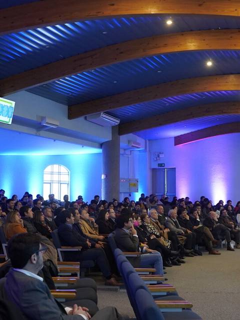 Una conferencia con un gran público escuchando al orador en un ambiente iluminado.