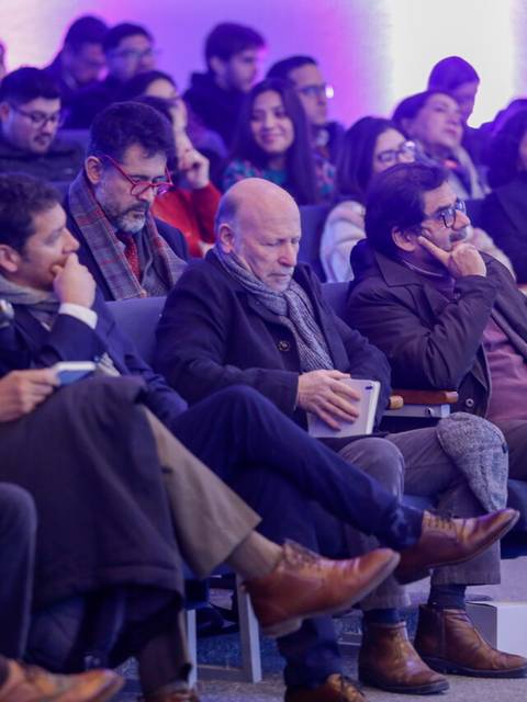 Un grupo de personas sentadas en un evento, escuchando atentamente en un ambiente iluminado.