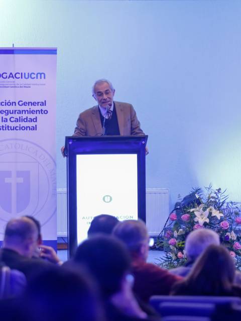 Un hombre mayor habla desde un podio en un evento ante un público atento.