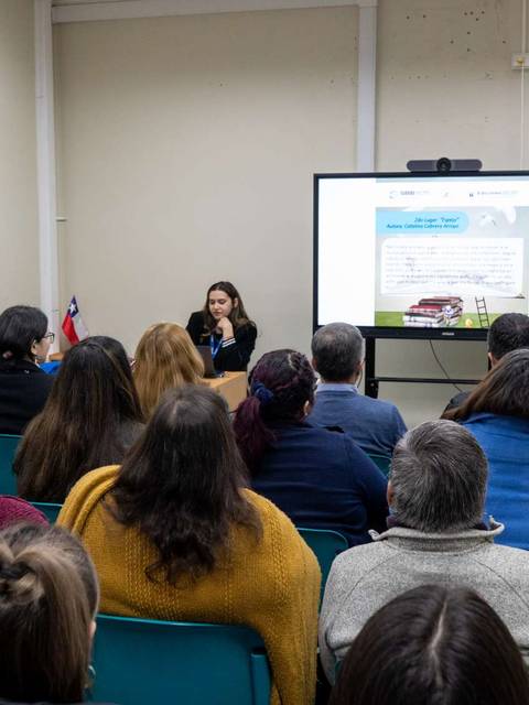 Una conferencia en un aula con una presentadora y un público atento.