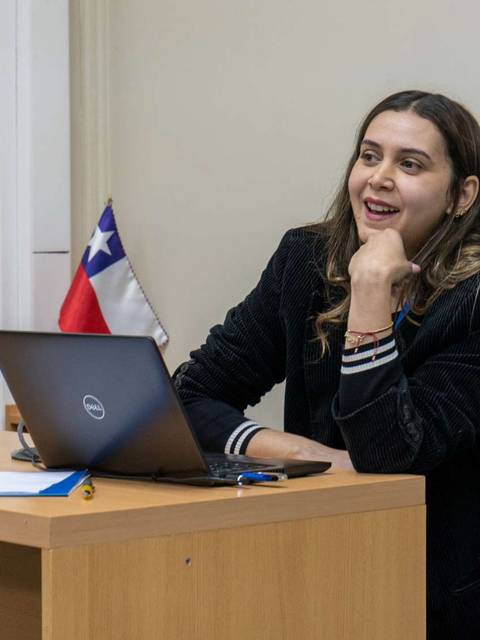 Una mujer sonriente se sienta frente a un ordenador portátil en un aula.