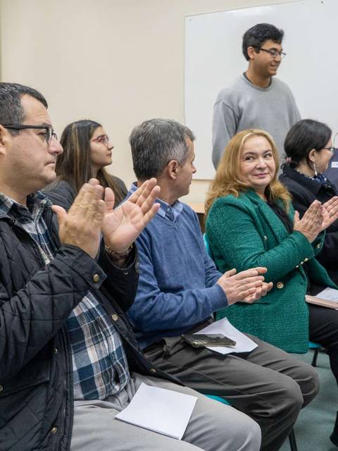 Un grupo de personas aplaude durante un evento, mientras un ponente se encuentra de pie al frente.