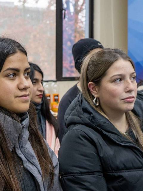 Grupo de jóvenes sentados en un ambiente interior, todos con abrigos oscuros y atentos.