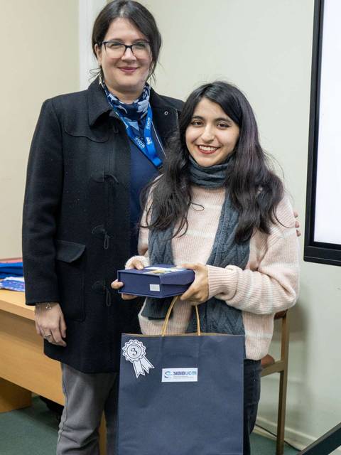 Dos mujeres sonríen, una sosteniendo una caja y la otra una bolsa, en un ambiente de celebración.
