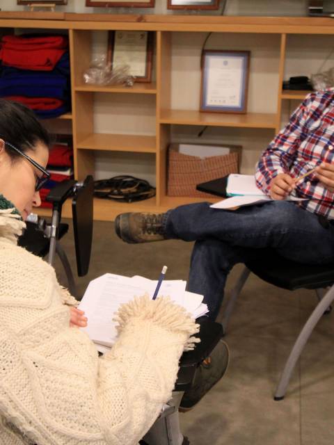 Dos personas interactuando en un entorno de estudio, una escribiendo y otra hablando.