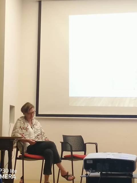 Una presentación en un espacio cerrado con dos personas sentadas en una mesa y una proyección en la pared detrás de ellas.