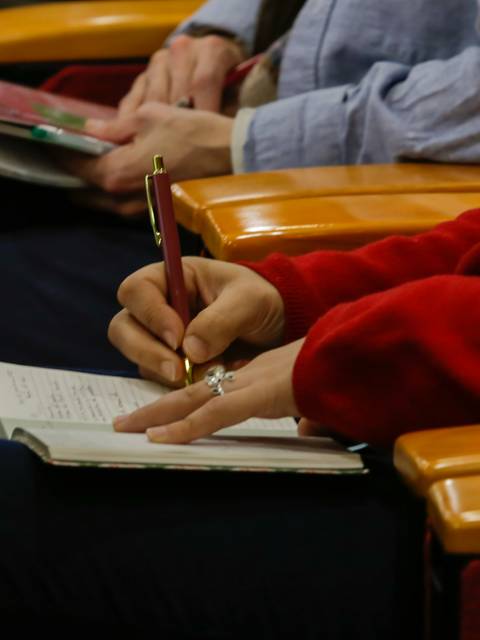 Una persona escribe en un cuaderno mientras se encuentra en un asiento de una sala.